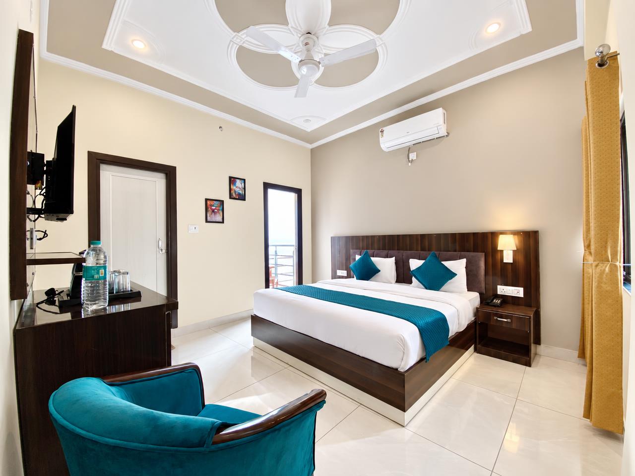 Deluxe room at Tapovan New Residency, Rishikesh — king bed with teal accents, TV and balcony door